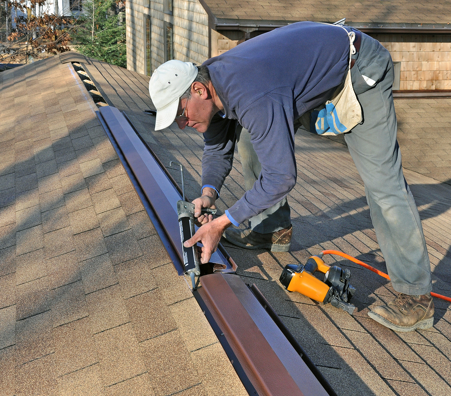 Carpenter applying caulk to ridge vent
